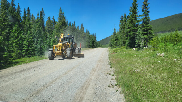ein Grader ebnet die Kiesstrasse, dahinter staubt es dann noch stärker...