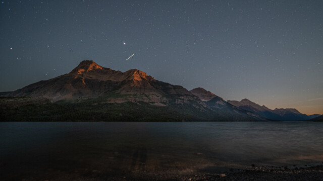Mondscheinfotografie, die Bergspitzen werden vom untergehenden Mond angeleuchtet, ĂĽber den Bergen noch eine Flugzeugspur als Strich